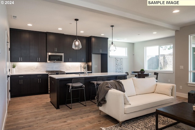 kitchen with light wood-type flooring, stainless steel appliances, pendant lighting, and an island with sink