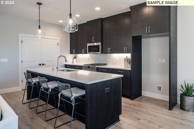 kitchen with appliances with stainless steel finishes, sink, decorative light fixtures, light hardwood / wood-style flooring, and a kitchen island with sink