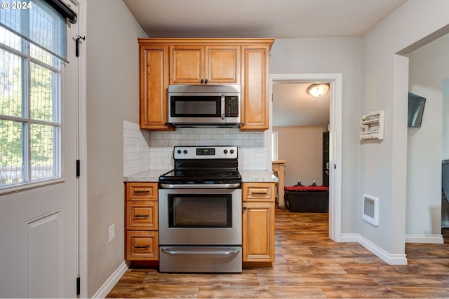 kitchen with decorative backsplash, stainless steel appliances, light stone counters, and light hardwood / wood-style floors