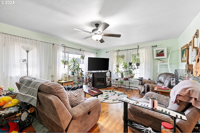 living area featuring light wood finished floors, a textured ceiling, a ceiling fan, and a glass covered fireplace