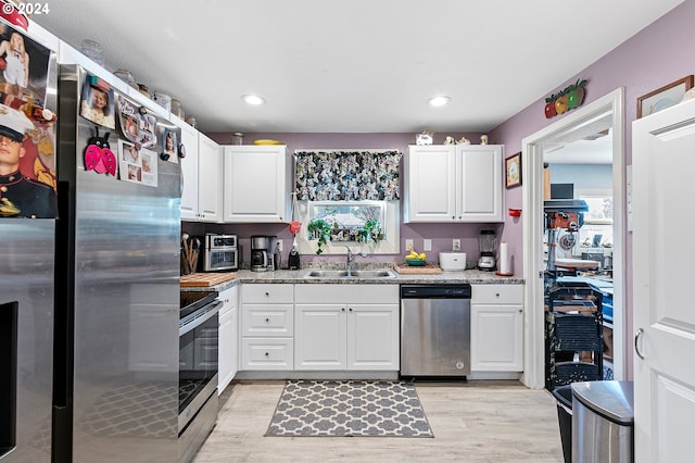 kitchen with light stone countertops, white cabinetry, stainless steel appliances, and a sink