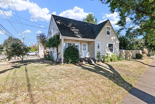 cape cod-style house with fence, a front lawn, and roof with shingles