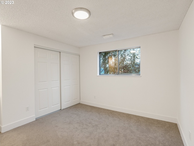 unfurnished bedroom featuring a textured ceiling, light carpet, and a closet