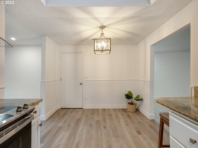 kitchen with light wood-type flooring, a textured ceiling, stone counters, and hanging light fixtures