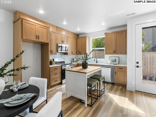 kitchen with a breakfast bar, light hardwood / wood-style floors, sink, decorative backsplash, and appliances with stainless steel finishes