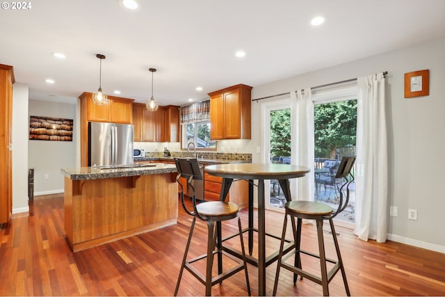 kitchen with stainless steel refrigerator, tasteful backsplash, a kitchen island, dark wood-type flooring, and pendant lighting