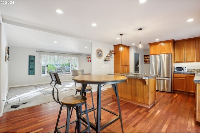 kitchen with a kitchen breakfast bar, hanging light fixtures, stainless steel refrigerator, and dark hardwood / wood-style flooring