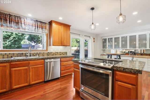 kitchen featuring sink, appliances with stainless steel finishes, hanging light fixtures, light hardwood / wood-style flooring, and decorative backsplash