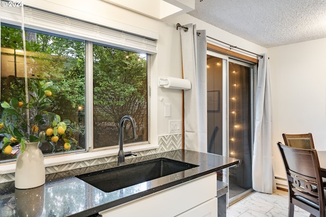 kitchen with dark stone countertops, white cabinetry, sink, and a textured ceiling