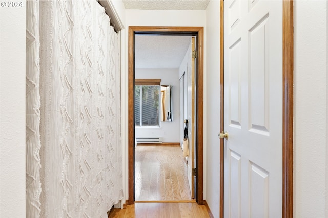 hallway featuring light wood-type flooring, a baseboard radiator, and a textured ceiling