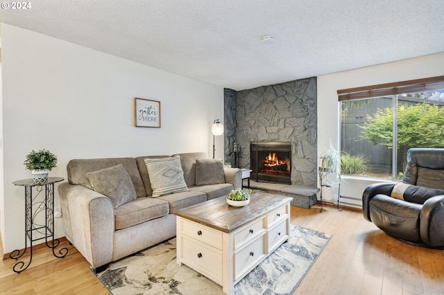 living room featuring a stone fireplace, a textured ceiling, and light wood-type flooring