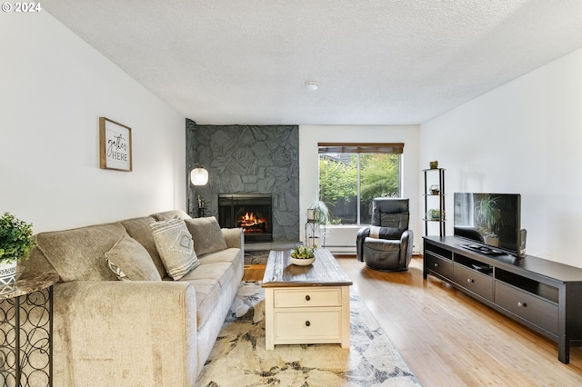 living room with light hardwood / wood-style floors, a textured ceiling, and a stone fireplace