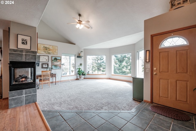 entrance foyer featuring ceiling fan, a tile fireplace, a wealth of natural light, and dark carpet