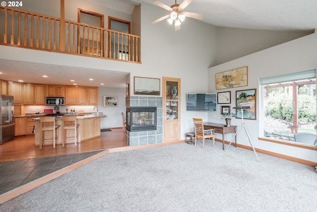 carpeted living room featuring a fireplace, high vaulted ceiling, and ceiling fan