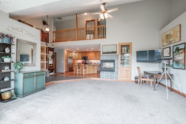 carpeted living room featuring ceiling fan, a towering ceiling, and a fireplace