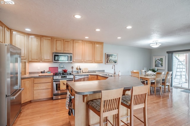 kitchen with stainless steel appliances, sink, light hardwood / wood-style floors, light brown cabinetry, and a breakfast bar