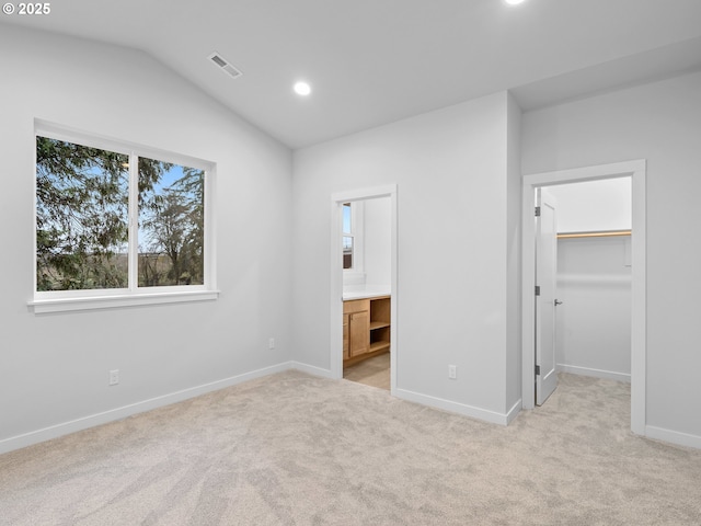 unfurnished bedroom with vaulted ceiling, a spacious closet, visible vents, and light colored carpet