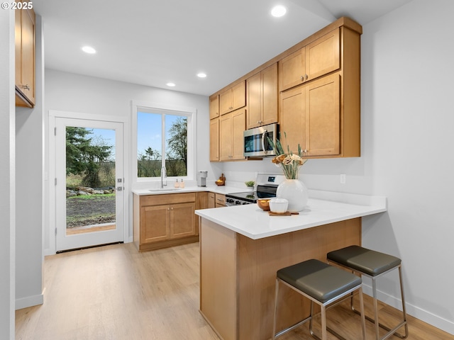 kitchen featuring a peninsula, light wood-style flooring, a breakfast bar, and stainless steel appliances