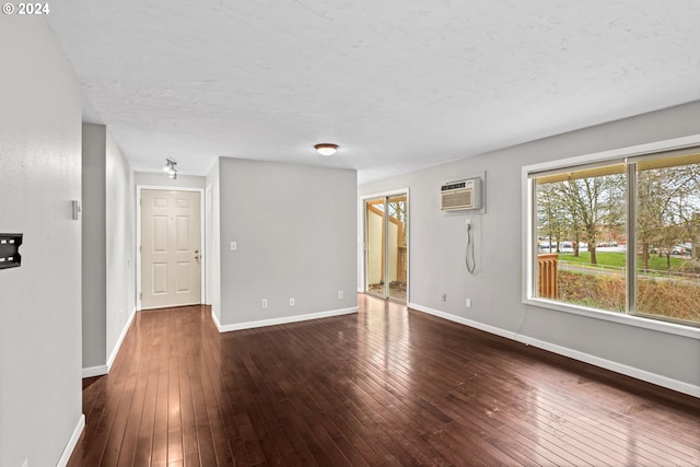 unfurnished room with a textured ceiling, a wall mounted air conditioner, and dark hardwood / wood-style floors