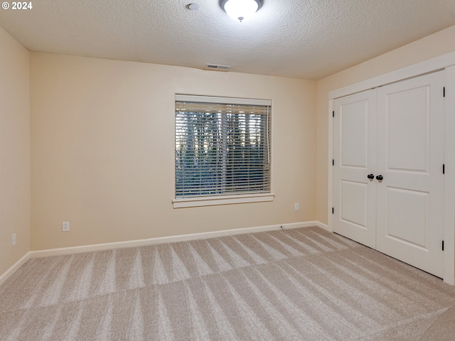 unfurnished bedroom with light carpet, a closet, and a textured ceiling