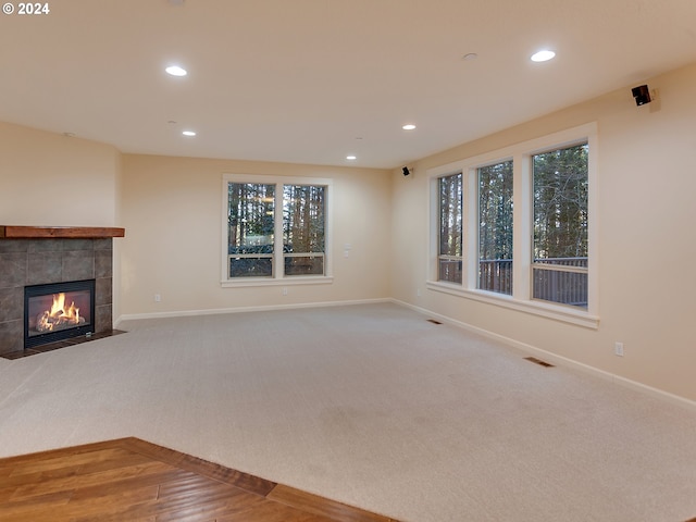 unfurnished living room with a tile fireplace, a wealth of natural light, and carpet floors