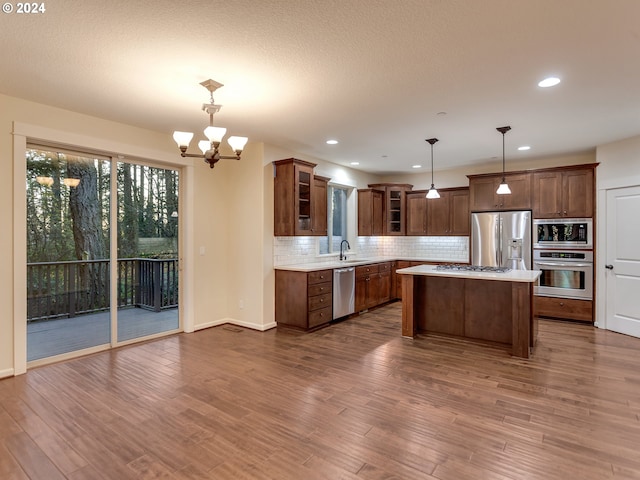 kitchen with appliances with stainless steel finishes, dark hardwood / wood-style flooring, pendant lighting, a chandelier, and a kitchen island