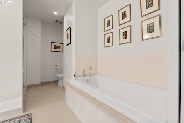 bathroom featuring tile patterned flooring, a relaxing tiled tub, and toilet