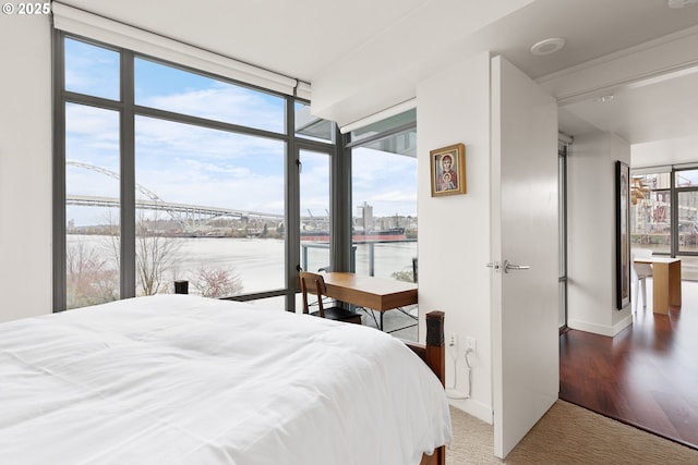 bedroom featuring hardwood / wood-style floors, floor to ceiling windows, a water view, and multiple windows