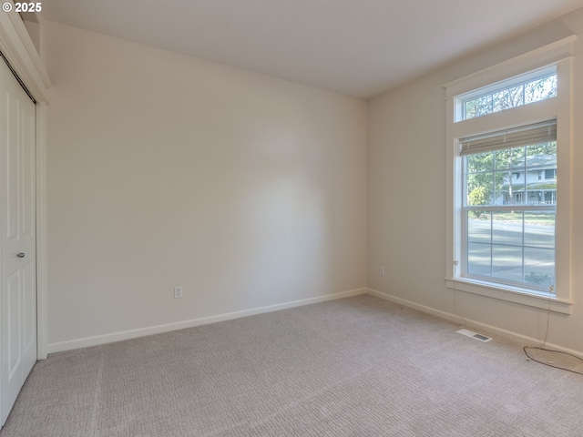 unfurnished bedroom featuring baseboards, a closet, light colored carpet, and visible vents