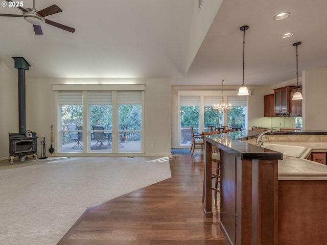kitchen with recessed lighting, dark wood finished floors, a wood stove, a sink, and ceiling fan with notable chandelier