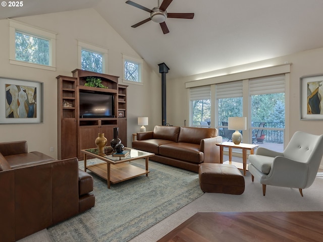 living room with high vaulted ceiling, plenty of natural light, a ceiling fan, and a wood stove