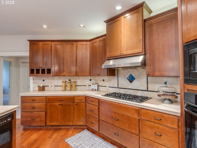 kitchen featuring light wood-type flooring, recessed lighting, decorative backsplash, under cabinet range hood, and black appliances