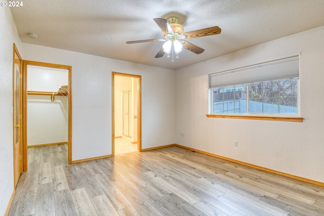 unfurnished bedroom featuring light wood-type flooring, a walk in closet, a textured ceiling, ceiling fan, and a closet