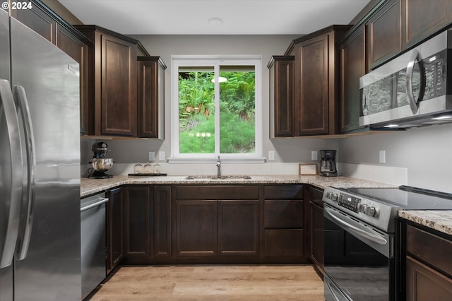 kitchen featuring dark brown cabinetry, light stone countertops, sink, appliances with stainless steel finishes, and light wood-type flooring