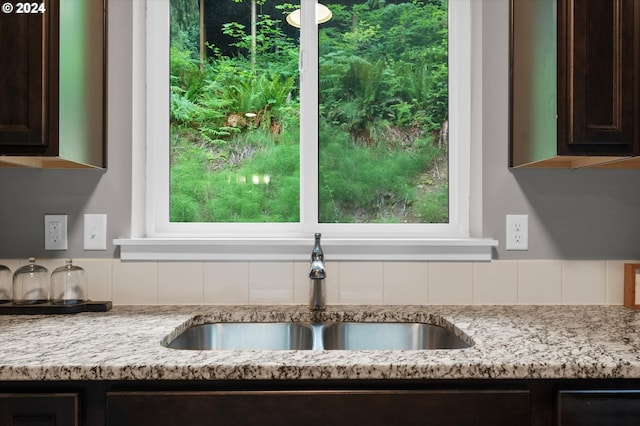 kitchen view of a sink, dark brown cabinetry, and light stone counters