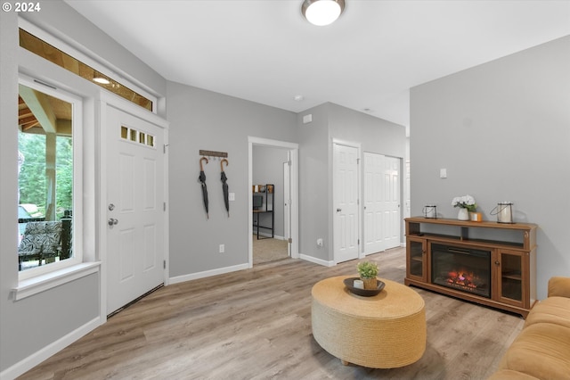 foyer entrance with light wood-style floors, baseboards, and a glass covered fireplace