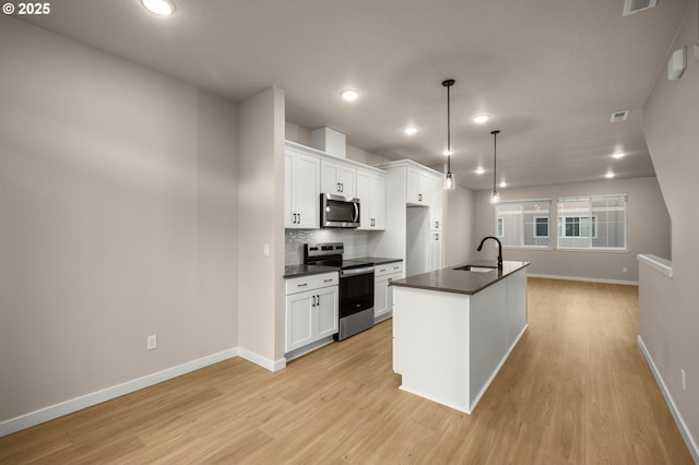 kitchen featuring dark countertops, light wood finished floors, decorative backsplash, appliances with stainless steel finishes, and white cabinets