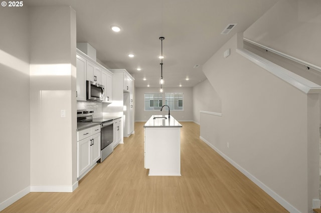 kitchen featuring light wood finished floors, white cabinets, appliances with stainless steel finishes, and an island with sink