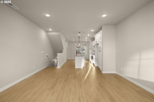 unfurnished living room with visible vents, light wood-style flooring, a sink, recessed lighting, and baseboards