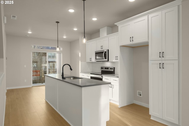 kitchen featuring a center island with sink, light wood finished floors, a sink, appliances with stainless steel finishes, and backsplash