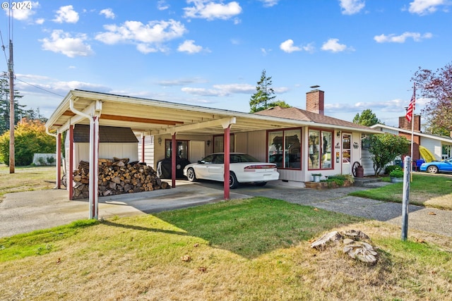 view of front of home featuring aphalt driveway, an attached carport, a chimney, and a front yard