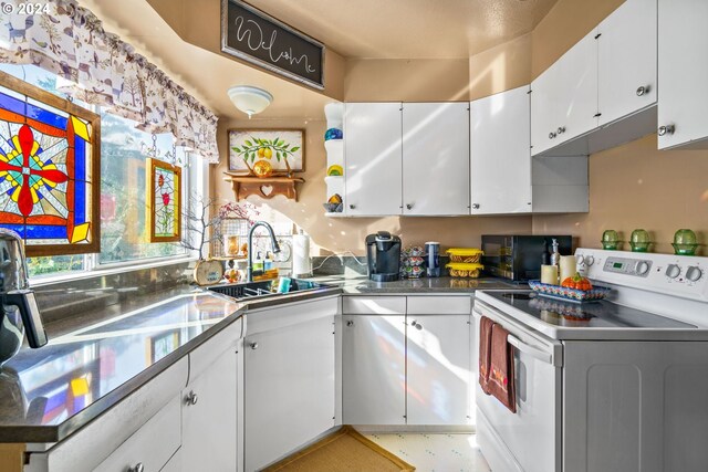 kitchen with stainless steel counters, sink, electric range, and white cabinets