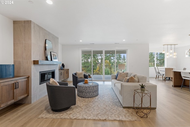 living room with a tiled fireplace, light hardwood / wood-style flooring, a healthy amount of sunlight, and tile walls