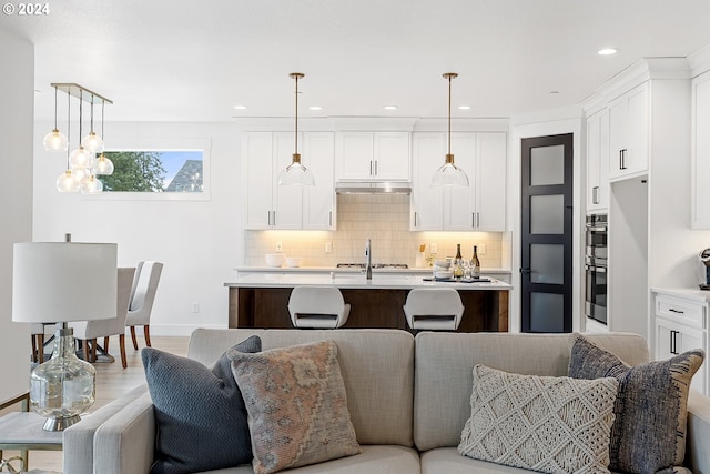 kitchen featuring white cabinets, backsplash, hanging light fixtures, and an island with sink