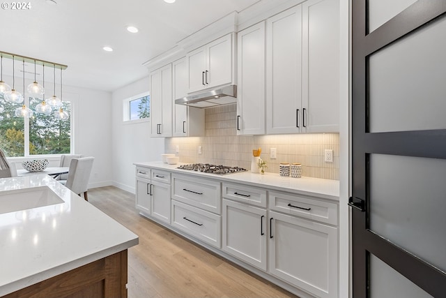 kitchen featuring white cabinetry, hanging light fixtures, tasteful backsplash, light hardwood / wood-style flooring, and stainless steel gas stovetop