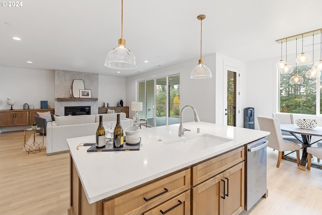 kitchen with a large fireplace, sink, an island with sink, pendant lighting, and light wood-type flooring