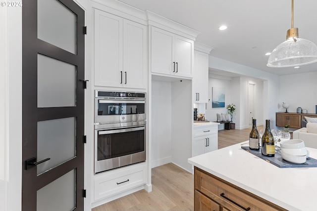 kitchen with white cabinets, decorative light fixtures, light hardwood / wood-style floors, and double oven