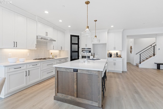 kitchen featuring light hardwood / wood-style flooring, white cabinets, decorative light fixtures, and stainless steel gas stovetop