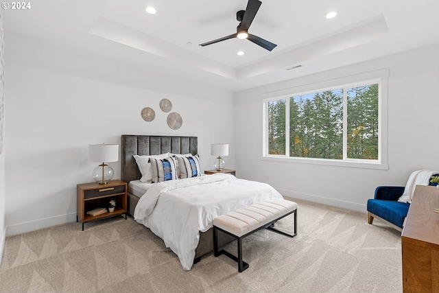 bedroom featuring light colored carpet, a raised ceiling, and ceiling fan