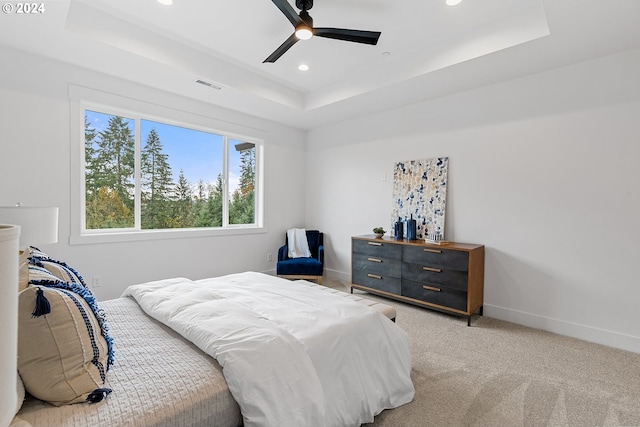 bedroom featuring light colored carpet, a raised ceiling, and ceiling fan